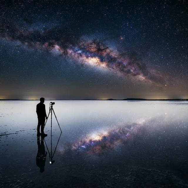 The Milky Way arching over the white salt flats of Rann of Kutch with a photographer's silhouette